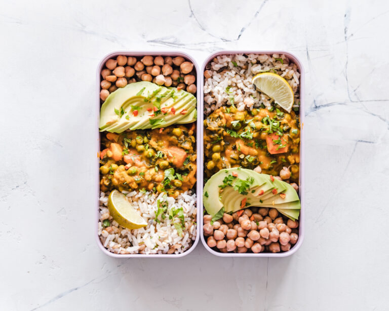Zwei gesunde Meal-Prep-Boxen mit Reis, Gemüsecurry, Kichererbsen und Avocado – vorbereitetes Essen für den Schichtdienst