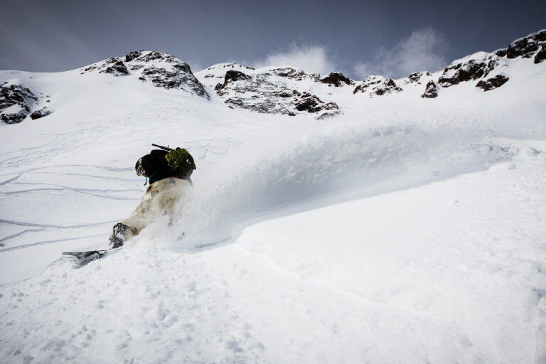 Skifahrer bei einem dynamischen Powder-Turn mit großer Schneefahne in hochalpiner Winterlandschaft